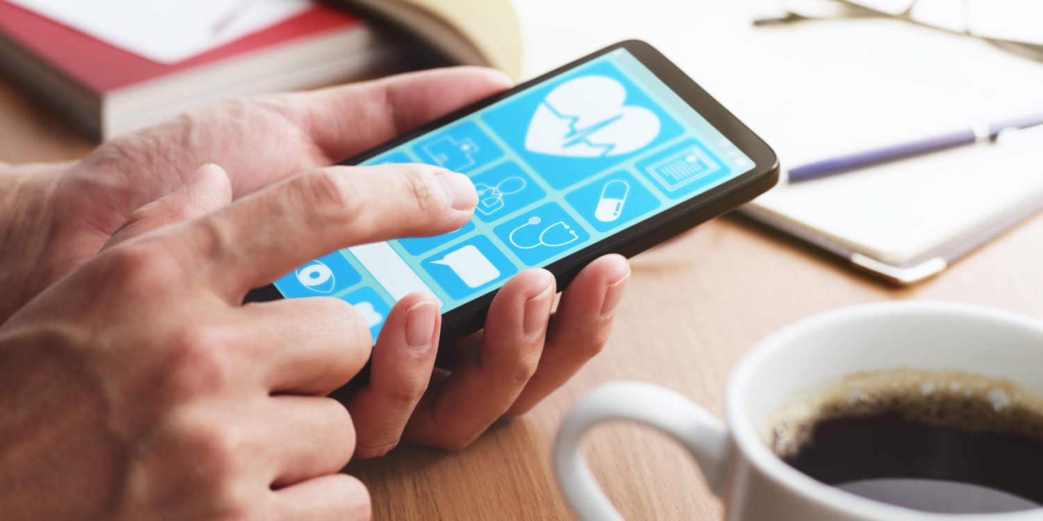 Online healthcare app on smartphone screen. Closeup of male hands touching smartphone screen at table.