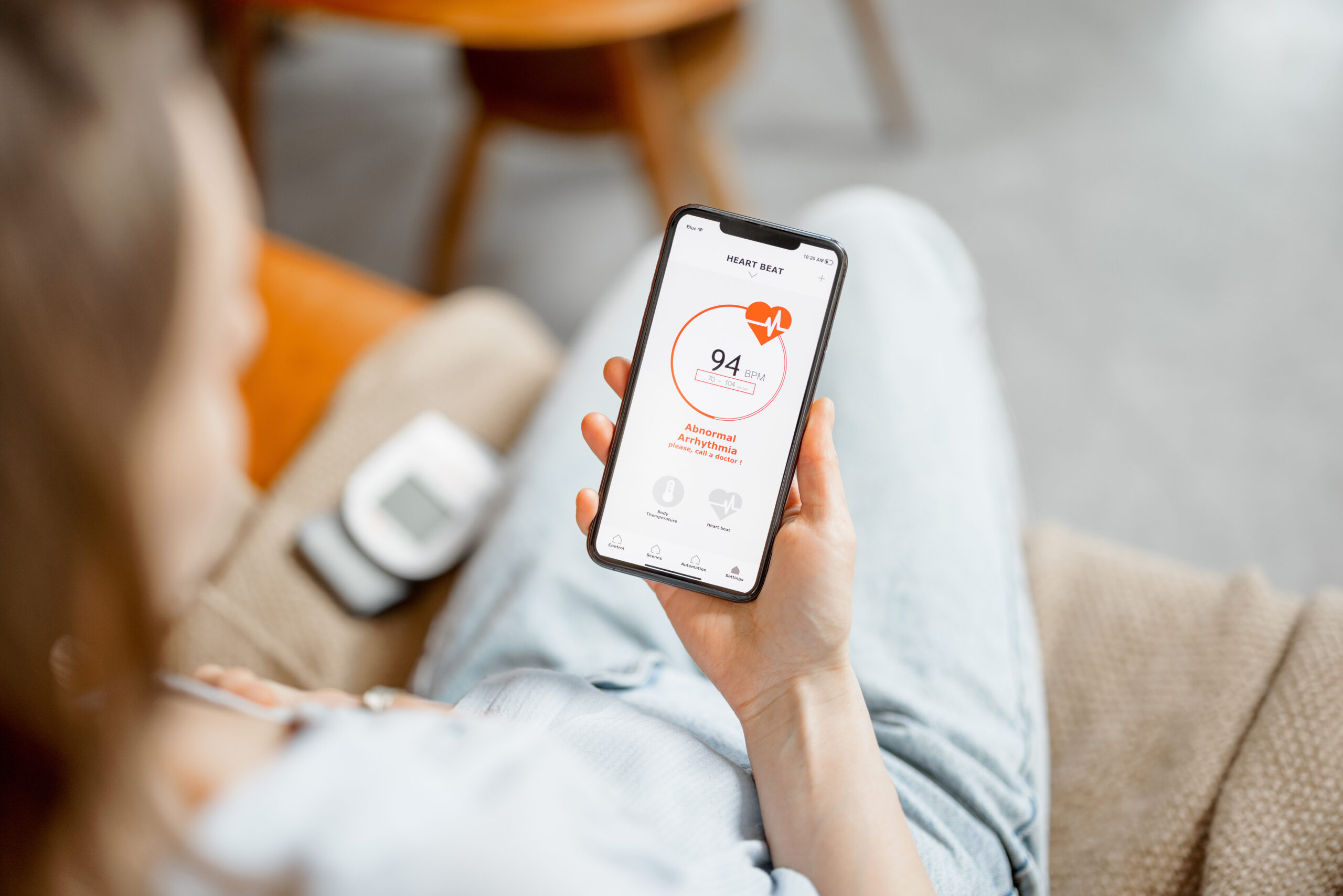 Woman measure heart rate with smart technology in phone while sitting on sofa at home. Health and wellness concept. Focus on phone screen